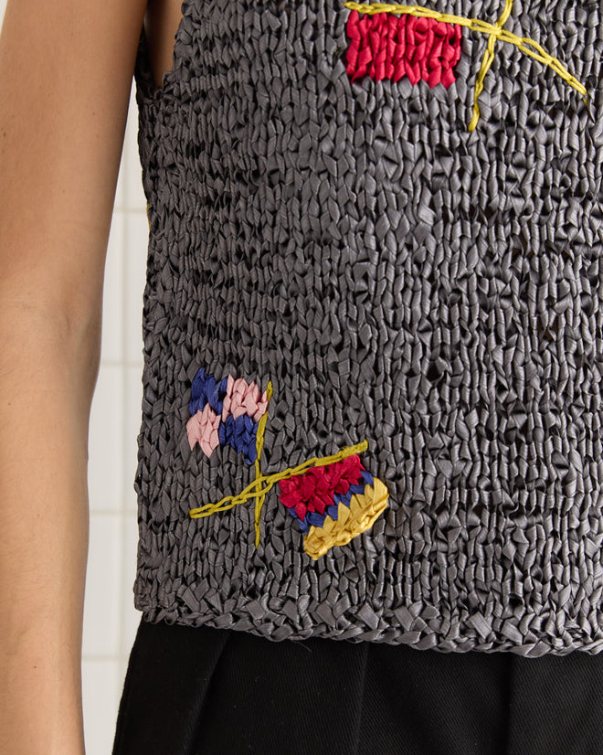 The Promenade Tank features a textured gray design with vibrant embroidery reminiscent of ribbonwork crochet, elegantly draped on the person's upper body.