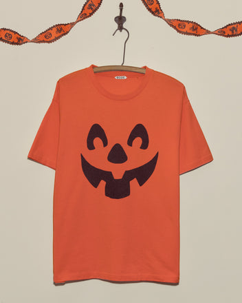 Pumpkin Tee with a bold black jack-o-lantern face, displayed on a hanger against a plain wall—perfect for fans of vintage Halloween shirts.