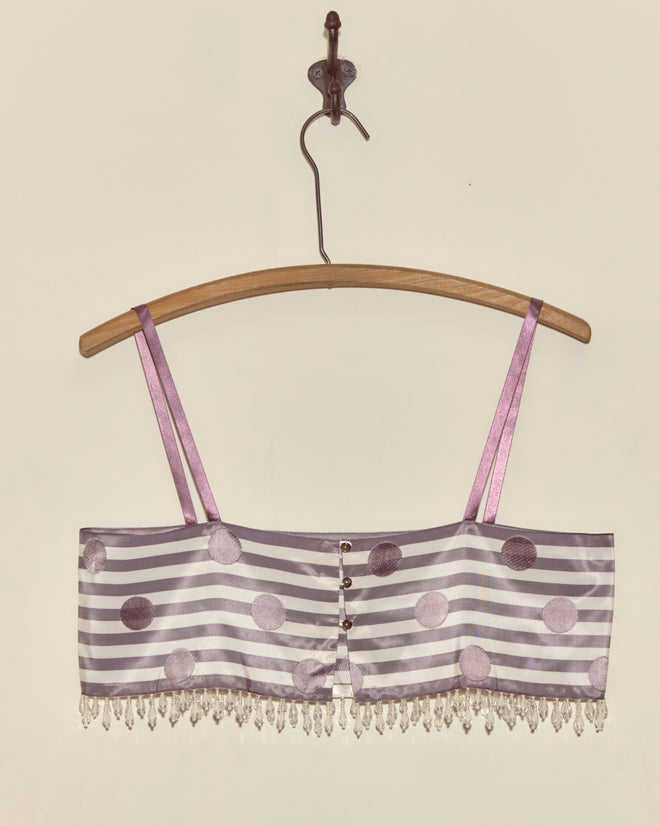 The Purple Note Bra - S is a lilac striped crop top featuring polka dots and bead fringe, crafted from Staron jacquard ribbons in a deadstock style, shown hanging on a wooden hanger against a plain wall.
