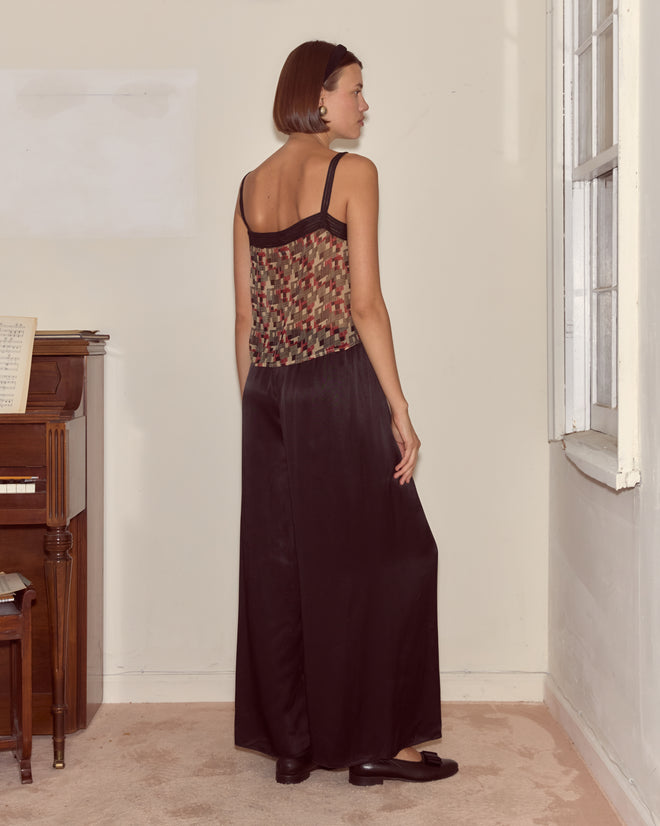 A woman wearing the Quadrille Tank and black pants stands in a room, facing away from the camera.