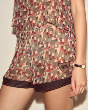 A person wearing Quadrille Tap Shorts and a watch, with only their lower torso and arm visible.