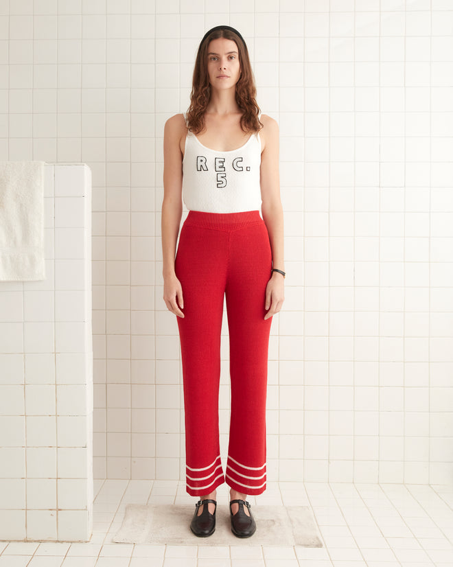 A woman in a white tank top and Quincy Stripe Joggers - Red stands in a tiled room, looking forward.