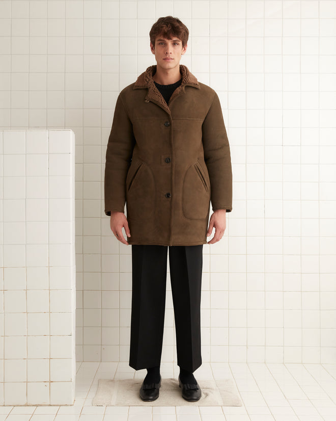 A person in a brown Ranch Coat and black pants stands in a tiled room with a neutral expression.