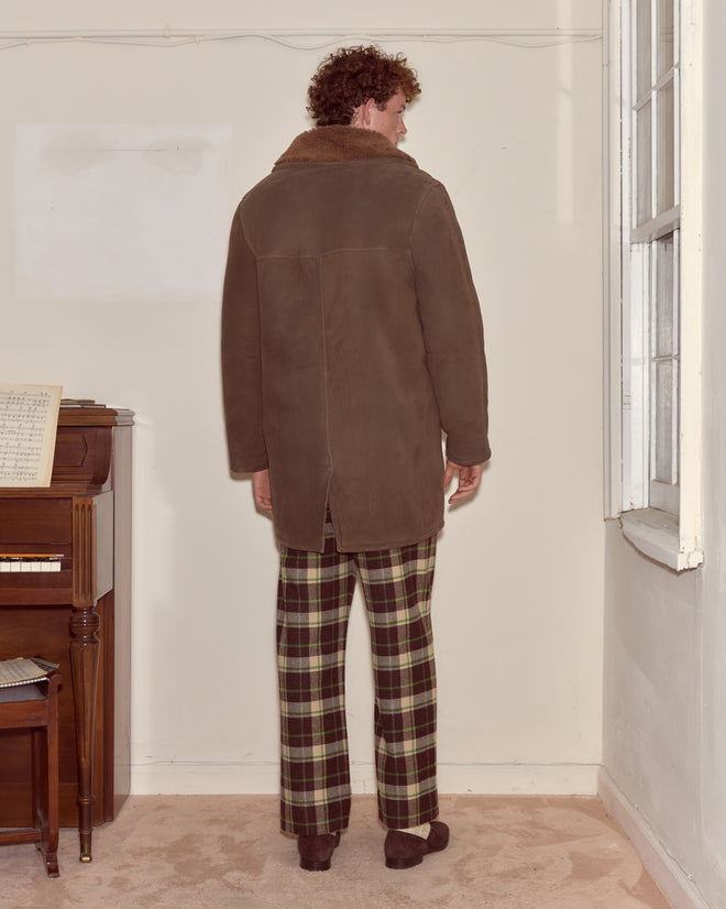A man wearing the Ranch Coat - Brown stands facing a cream wall near a piano and window.