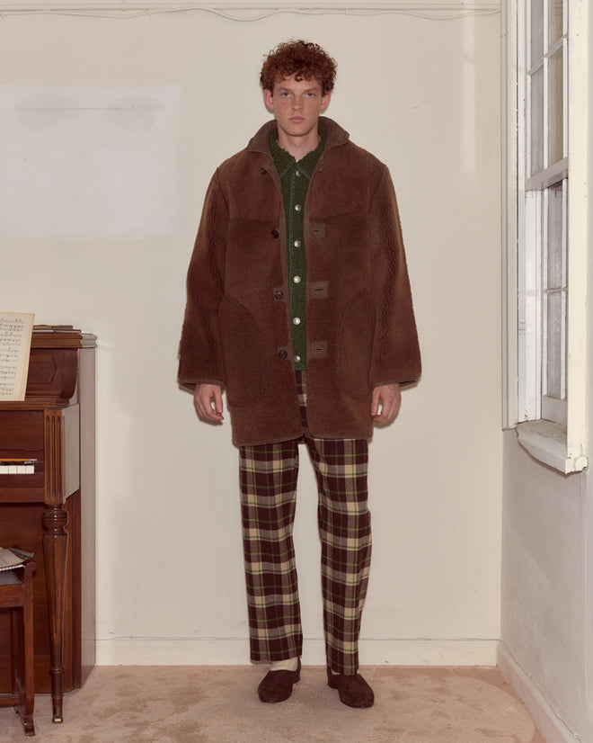 A man in a Ranch Coat - Brown and plaid pants stands indoors beside a piano and window.