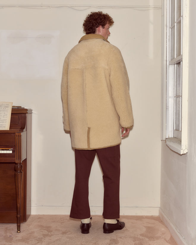 A man with curly hair wears the Ranch Coat and brown pants, standing facing a wall in a vintage 1950s-inspired room.