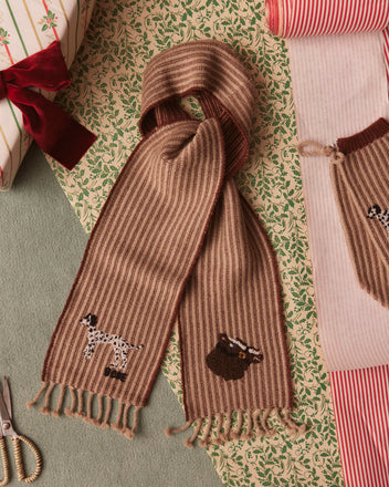 The Ranch Scarf, inspired by 1970s design, features brown stripes with charming dog and bear patterns. Crafted from 100% wool, it is beautifully accompanied by gift wrapping paper and scissors.