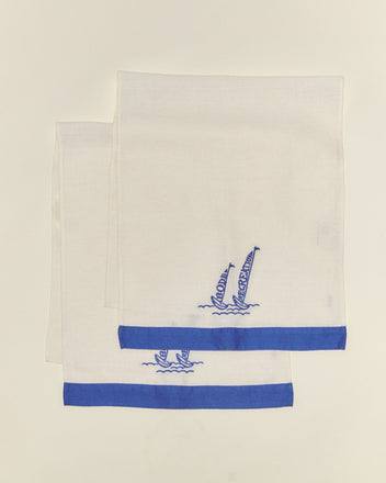 Two Recreation Sails Dish Towels, made of lightweight linen with blue borders and embroidered sailboats in one corner, are displayed on a plain background.