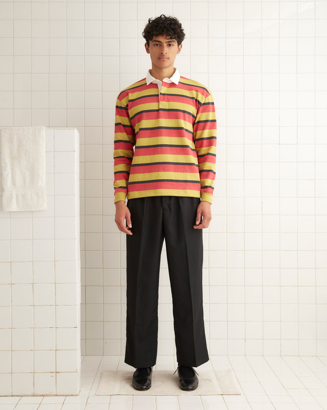 A person in a Rec Stripe Polo of heavyweight cotton and black pants stands confidently in a tiled room, capturing a timeless 1980s reproduction vibe.