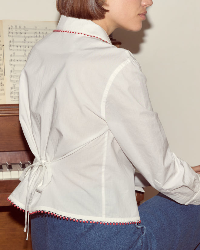 A woman in a Redbud Top sits at a piano with sheet music, facing away from the camera.