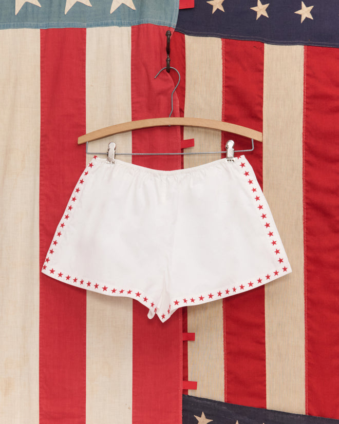 Red Star Tap Shorts hang in front of a vintage American flag—ideal for Liberty costumes or Fourth of July celebrations.