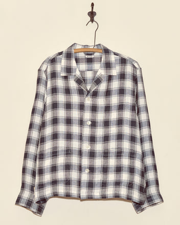 The Reeves Check Long Sleeve Shirt - L features unique black and white plaid deadstock suiting wool, displayed on a wooden hanger against a beige wall.