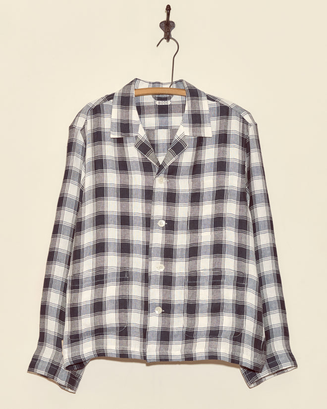 The Reeves Check Long Sleeve Shirt - L features unique black and white plaid deadstock suiting wool, displayed on a wooden hanger against a beige wall.