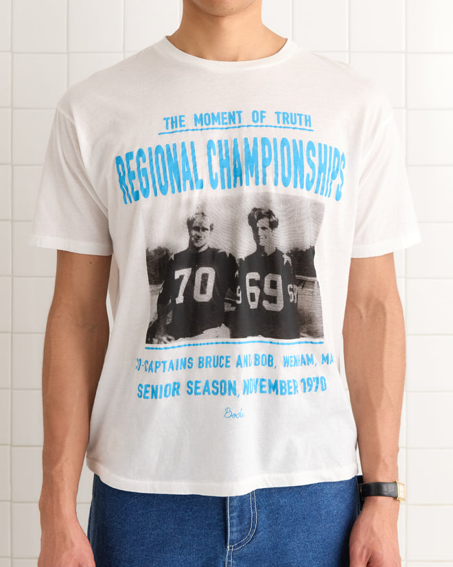 A person wearing the Regionals Tee, a white vintage-weight cotton t-shirt featuring a vintage sports "Regional Championships" print and player photos, inspired by classic commemorative tournament shirts.