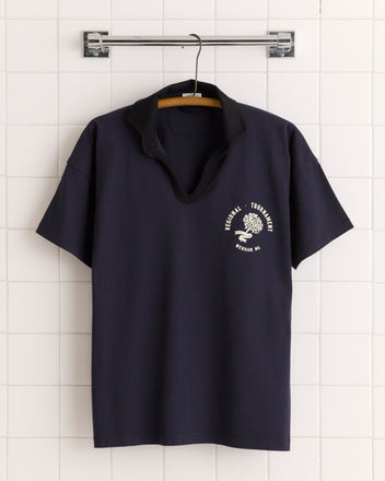 Regionals Polo: Navy blue 100% cotton polo T-shirt with black collar, white logo, and text, displayed on a hanger against a tiled wall.