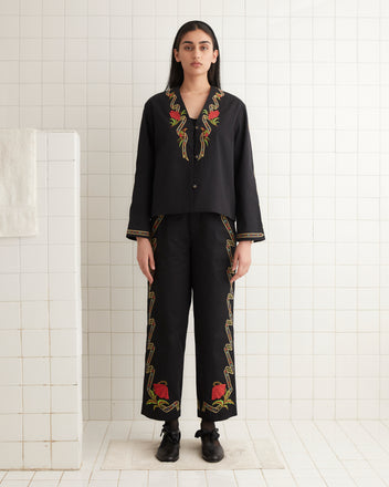 A woman wearing a Ribboned Hollyhock Jacket stands in a tiled room, facing forward.