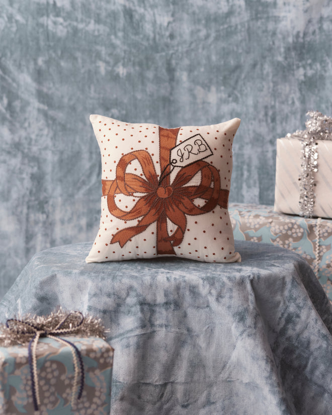 The Ribbon Pillow - Brown is elegantly displayed on the table, surrounded by gift boxes, adding a charming touch to your collection of elegant home goods.