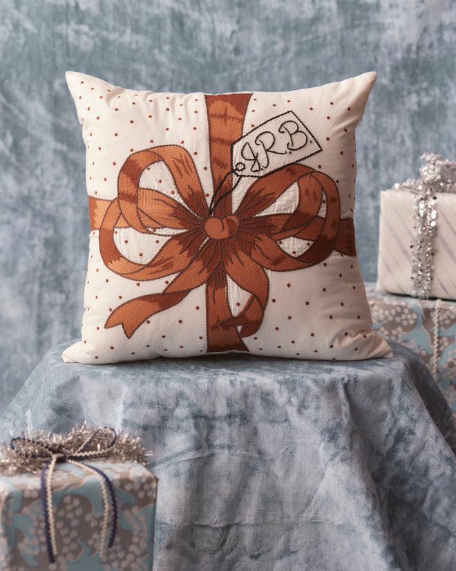 The Ribbon Pillow - Brown is elegantly displayed on the table, surrounded by gift boxes, adding a charming touch to your collection of elegant home goods.