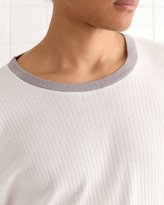 A person shown from the shoulders up wears the Rib Boxy Tee, a ribbed light beige top with a grey ringer neckline, made from 100% cotton.