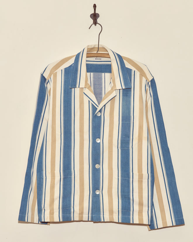 The Riverbed Stripe Long Sleeve Shirt - XL features blue, white, and beige vertical stripes and hangs on a wall hook.
