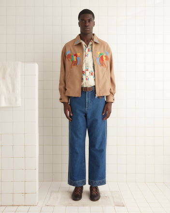 A man stands in a tiled room wearing the Rodeo Ohio Jacket over a patterned shirt, blue jeans with decorative cuffs, and brown shoes.