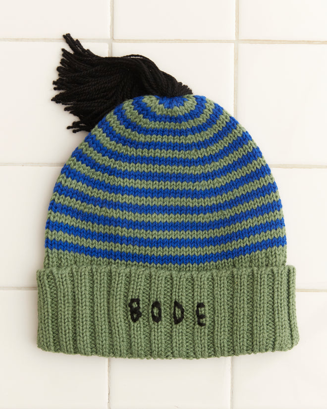 The Roll-Up Tassel Beanie in green is a vintage-style striped beanie made from soft merino wool, highlighted with a black tassel and an embroidered 