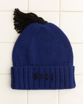 The Roll-Up Tassel Beanie - Navy, a vintage children's hat made from soft merino wool, showcases a blue knit design with a black tassel and 