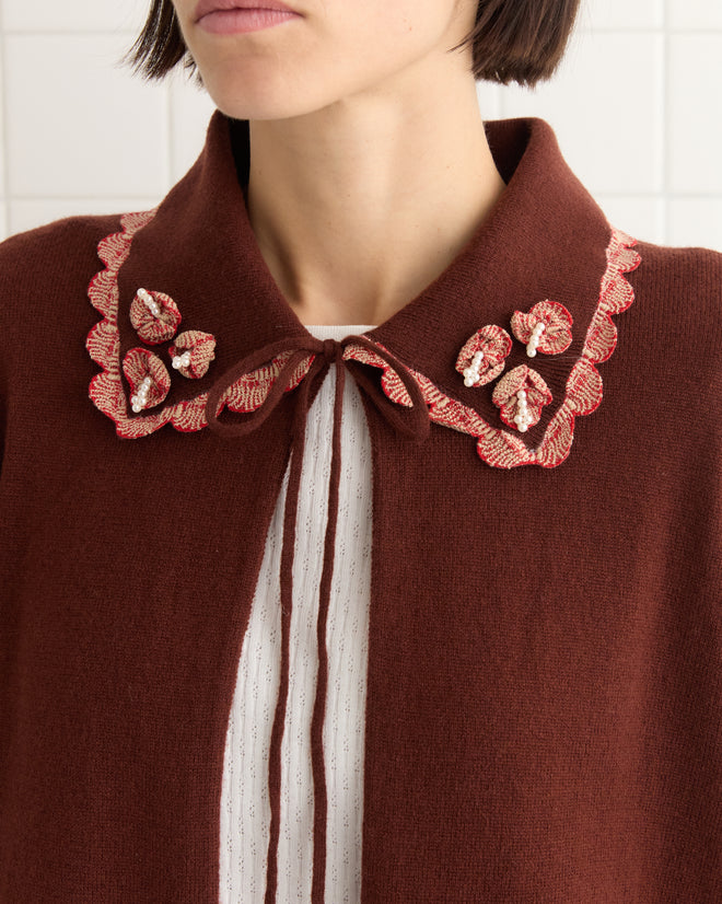 A person models a white shirt topped with a brown scalloped collar featuring floral embroidery, which is highlighted by the candy-striped trim of their cozy Rookie Cardigan.