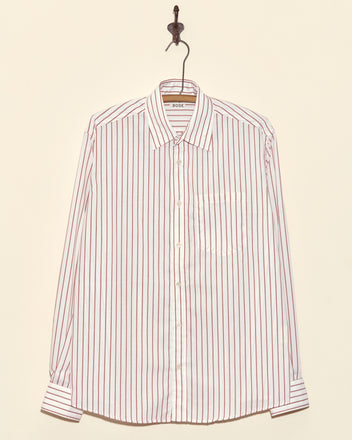 Rosetta Stripe Shirt - BROWN with vertical stripes hangs on a hook against a beige wall—this classic women's shirt brings effortless style to any wardrobe.