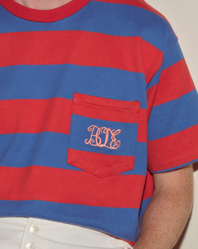 Wearing the Clubhouse Tee—a red and blue striped, 100% cotton shirt with a pocket, embroidered with curly "RCY" initials for added style and comfort.