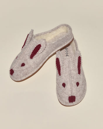 The Rabbit Slipper is a pair of fuzzy, fleece-lined slippers with a cream base, styled as white rabbits and detailed with maroon ears and noses.