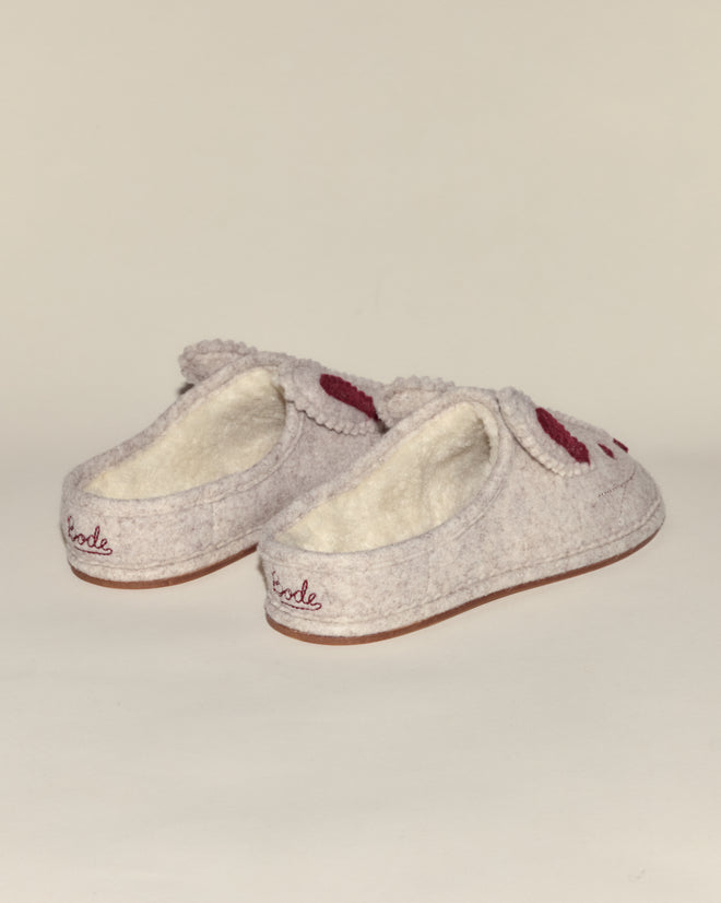 Rabbit Slipper - Cream Red: a pair of fuzzy, cream-colored slippers with red accents and embroidered text on the heels, displayed on a plain background.