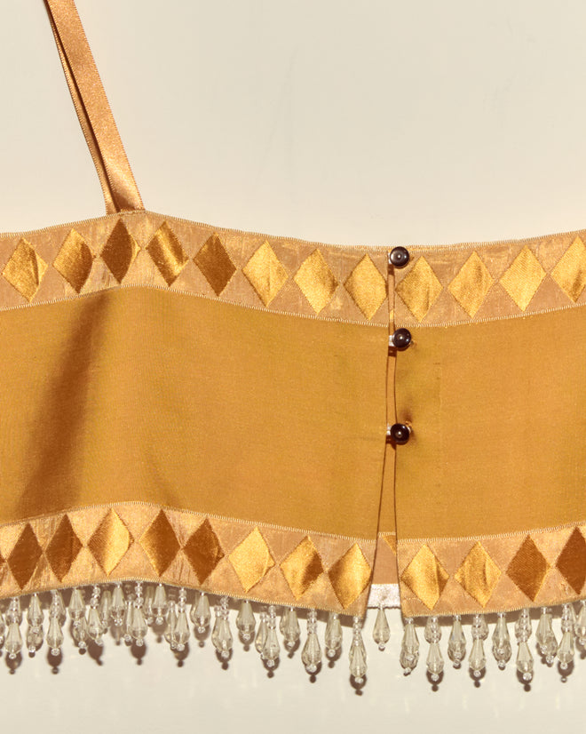 The Saffron Pierrot Bra - S features gold fabric with diamond patterns, clear beaded fringe, button details, French couture textile, and Staron jacquard ribbons, all set against a plain light background.