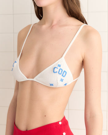 A person wearing a Sailfish Bra bikini top and red bottoms stands against a tiled wall, subtly elevated by Cape Cod detailing.