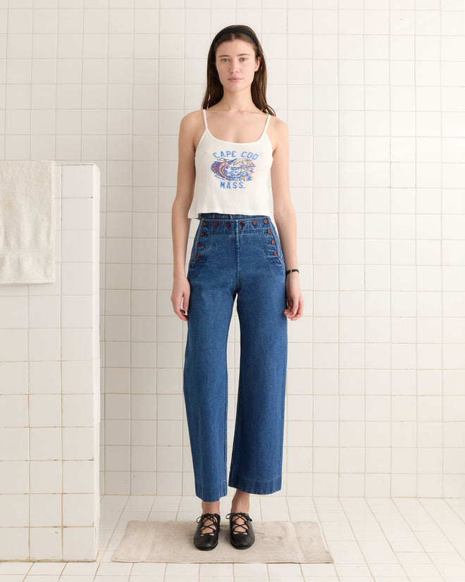 A person wearing a Beaded Sailfish Tank and blue jeans is standing in a tiled room with a hanging towel.