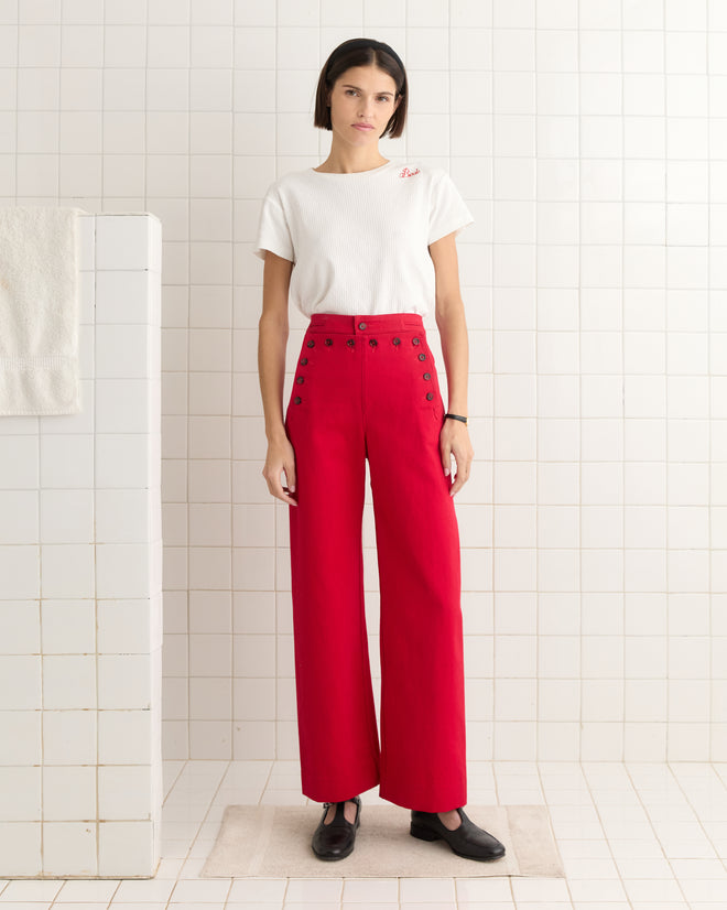 A person in a white shirt and Spring Twill Sailor Trousers stands in a tiled room with a towel on the left.