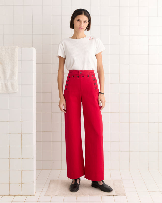 A person in a white t-shirt and Spring Twill Sailor Trousers stands on a rug in a white-tiled room.