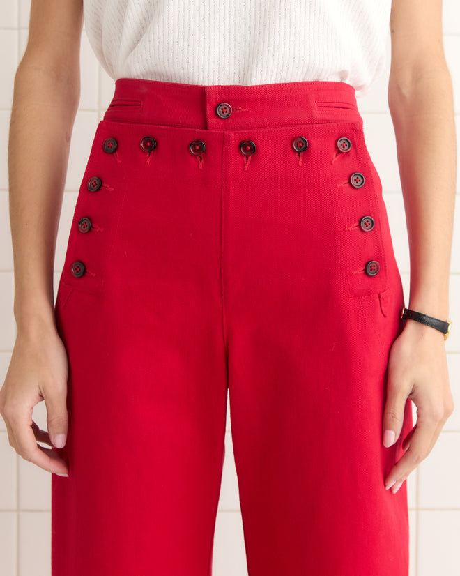 Someone elegantly wearing high-waisted Spring Twill Sailor Trousers in red cotton with button details, paired with a crisp white top.