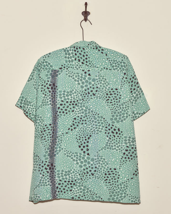 The Sardine School Shirt - XXL, a light green vintage shirt with a dotted pattern and short sleeves, hangs on a wall hook.