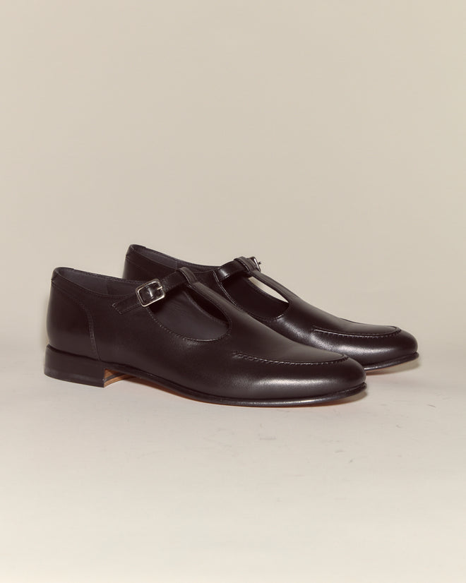 The School Shoes - Black are black leather T-strap shoes with buckles, made in Italy and shown on a neutral background.