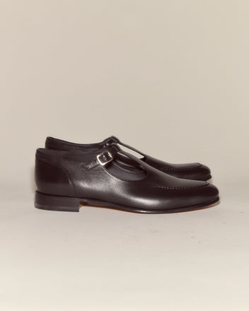 School Shoes - Black: Classic Italian-made black leather shoes with a side buckle in T-strap style, displayed on a neutral background.