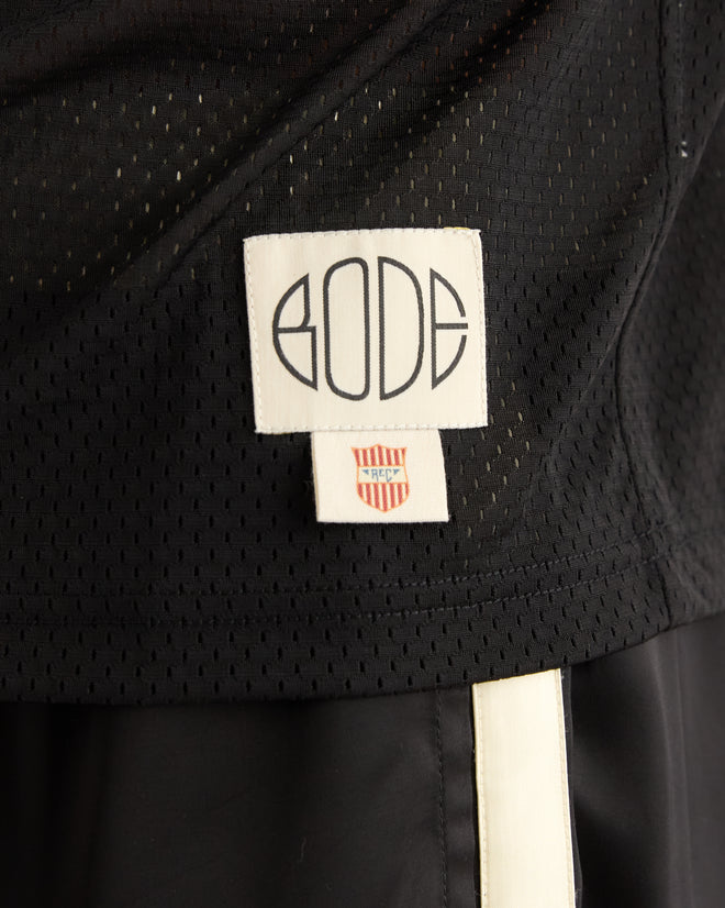 Close-up of the Scrimmage Jersey - Black, featuring a white "BODE" tag and a small red and white shield logo, resembling a classic black mesh football practice jersey.