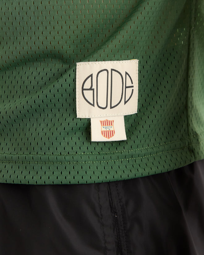 Close-up of the Scrimmage Jersey - Green featuring a white "BODE" label and a small red and yellow shield tag beneath it.