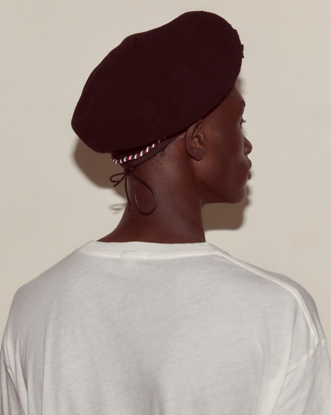 A person seen from behind in a white shirt wears the Script Beret—Black with Red/Blue Piping, made in France from 100% wool.