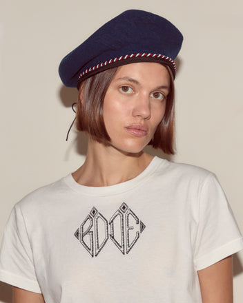 Woman with short brown hair wears the Script Beret in navy with red/blue piping and a white 