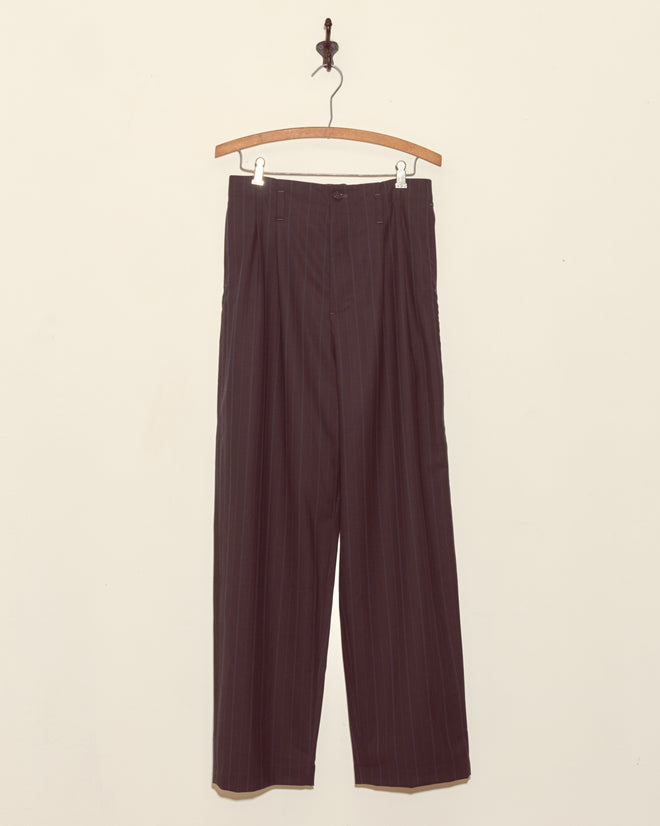 Sea Levels Trousers - 28 in dark pinstriped deadstock wool hang on a wooden hanger against a plain off-white wall.