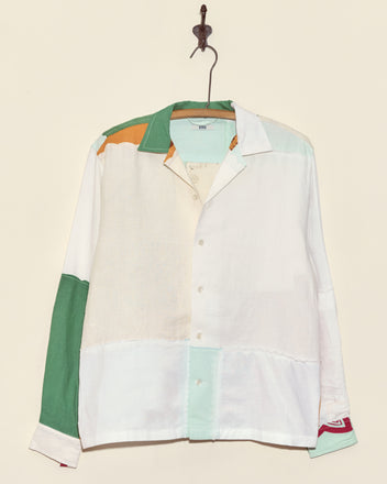 The Seashore Napkin Shirt - S/M, a unique colorblock button-up in green, white, orange, and mint panels made from vintage napkins, hangs on a hook against a beige wall.