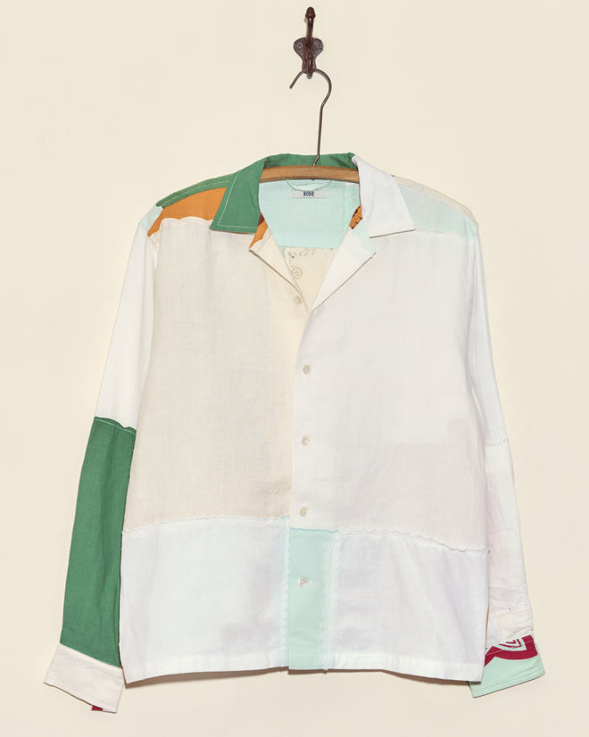 The Seashore Napkin Shirt - S/M, a unique colorblock button-up in green, white, orange, and mint panels made from vintage napkins, hangs on a hook against a beige wall.