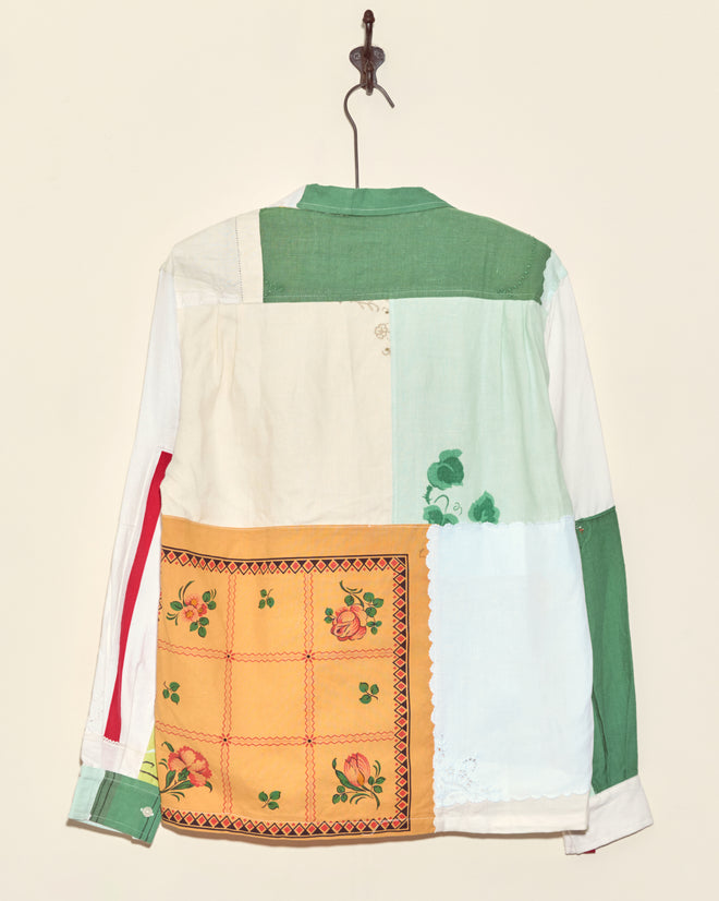 The Seashore Napkin Shirt - S/M features unique green, white, and yellow floral patchwork panels, made from vintage napkin fabric in New York, shown hanging on a hook.