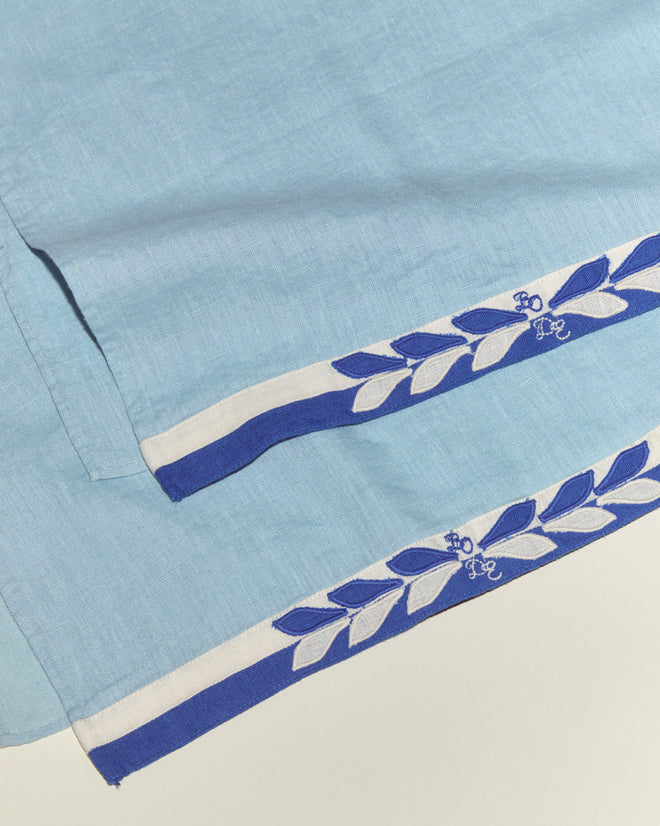 The Seedling Stripe Dish Towels are light blue linen towels with a blue and white leaf-patterned border and small embroidered blue flowers, inspired by classic midcentury dishtowels.